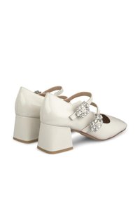 White patent leather block-heel shoes with pointed toes, featuring dual buckle straps adorned with rhinestones and a smooth, glossy finish.