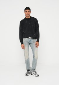 Fekete kötött pulóver kerek nyakkivágással, világoskék kopott farmer, fekete-fehér, elegáns kialakítású tornacipő.