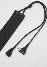 Correa de cuero negro con una superficie texturizada, que presenta dos borlas en los extremos. Ajustable con un cierre de cordón y herrajes de metal.