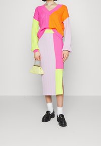 Zestaw z dzianiny, sweter i spódnica, w kolorach różowym, pomarańczowym, zielonym i lawendowym. Wyróżnia się dekoltem w serek, prążkowaną fakturą i ozdobnym paskiem. Do kompletu mała torebka.