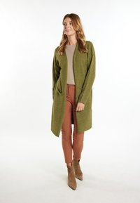 Cardigan lungo e aperto davanti di colore verde oliva, realizzato in tessuto a maglia testurizzato, abbinato a pantaloni marroni aderenti e stivaletti alla caviglia taupe.