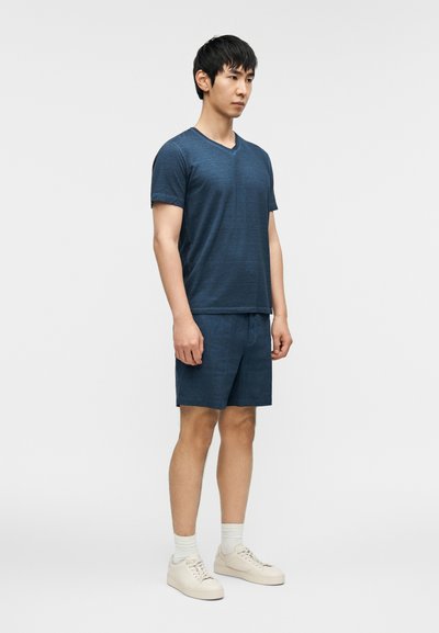 Μπλε ναυτικού χρώματος κοντομάνικο μπλουζάκι με V λαιμόκοψη, σετ με αντίστοιχα σορτς, με άνετη εφαρμογή και διακριτική υφή. Συμπληρώνεται με ανοιχτόχρωμα αθλητικά παπούτσια.