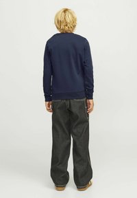 Navy blue sweatshirt with a round neck, ribbed cuffs, and hem. Paired with loose-fitting, dark gray jeans and beige shoes, viewed from behind.