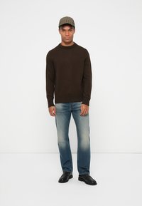 Brun stickad tröja med ribbad halsringning, tillsammans med ljusblå raka jeans. Svarta skor och en rutig keps fulländar outfiten.