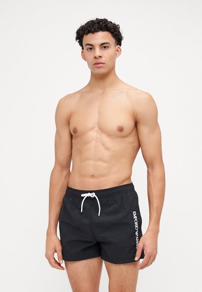 Shorts de bain noirs en tissu texturé, avec une taille élastique et un cordon de serrage blanc. Présente un logo blanc sur le côté.