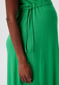 Vestido verde hecho de tejido ligero, con cintura ajustable de cordón. La textura es suave y el color es vibrante y uniforme.