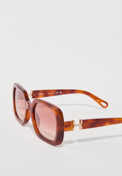 Gafas de sol de acetato marrón con grandes monturas rectangulares, lentes rosa degradado y acentos de hardware dorado en las patillas.