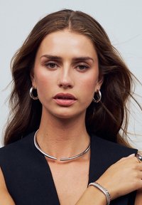 Silver smycken som har en böjd choker och ringörhängen. Slät metallisk yta, minimalistisk design, bärs med en mörk topp.