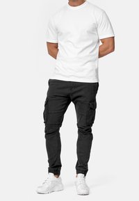 T-shirt bianco a girocollo abbinato a joggers cargo neri con tasche laterali, polsini elastici e sneakers nere. Design casual e aderente.