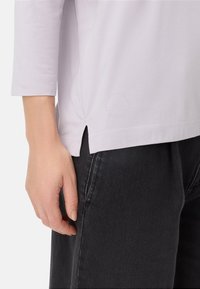 Licht laveren langemouwtop met zijsplits en een subtiele gebosselde logo op de zoom, gecombineerd met donkergrijze denim broek.