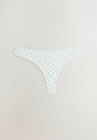 Chiloti tip tanga albi pentru femei, cu model mic de inimioare negre și o fundiță mică în centrul taliei, așezați pe o suprafață plană, pe un fundal deschis.