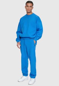 Blauer Pullover und passende Jogginghosen, beide aus weichem Stoff gefertigt. Der Pullover hat einen Rundhalsausschnitt; die Jogginghosen verfügen über seitliche Taschen und eine schmal zulaufende Passform.