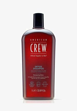 Rød plastflaske med sort flip-top låg, mærket "DETOX SHAMPOO," indeholder 1 liter shampoo med oplysninger om vegansk og silikonefri formel.