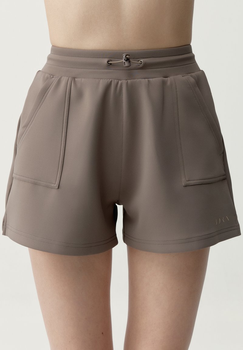 Taupekleurige shorts met hoge taille, voorzakken en verstelbaar trekkoord, gedragen door een persoon tegen een effen achtergrond.