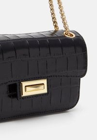 Černá kabelka z umělé krokodýlí kůže se zlatým řetízkovým popruhem. Má obdélníkový tvar a lesklou texturu se zlatým zapínáním.