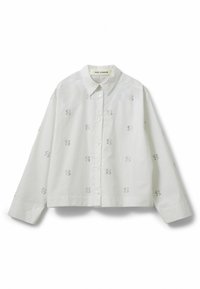 Hvid, langærmet bluse med krave og knaplukning foran. Har broderede mønstre i et subtilt design hele vejen igennem. Skræddersyet pasform.