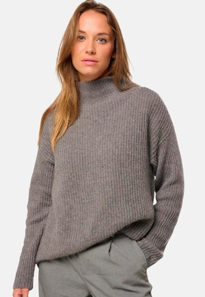 Pull en maille côtelée gris avec un col montant, des manches longues et une coupe décontractée. Il présente une texture douce et une légère variation de couleur.