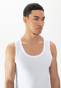 Witte mesh tanktop met brede bandjes en een ronde halslijn. Heeft een textuurstof en een aansluitende pasvorm.