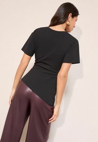 Mustast lühikeste varrukatega top, millel on kehajäärdis disain ja ümmargune kaelus, kombineeritud läikivate bordoopunaste laia sääre pükstega, mis näitavad sujuvaid tekstuure.