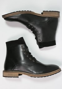 Mustat nahka nilkkurit, joissa on pyöreä varvas, nauhoitus edessä ja kahden sävyn puukorko. Varustettu mokkanahkakauluksella ja metallisilla rei'illä.