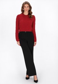 Czerwony sweter dziany z teksturowym wzorem i ozdobami, zestawiony z czarnymi spodniami o wysokim stanie i czarnymi szpilkami.