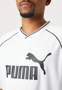 White sports jersey made of breathable fabric featuring a black Puma logo and accents. V-neck design with black trim and textured material.