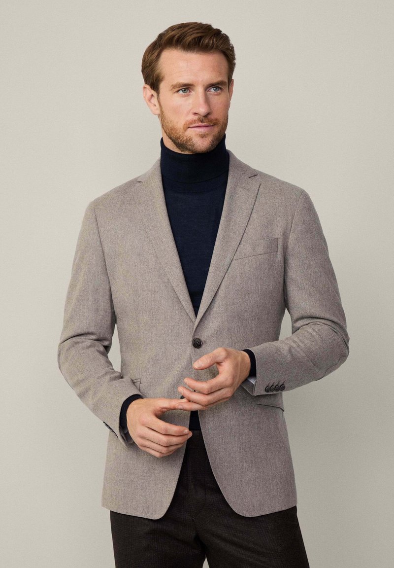 Ljusgrå blazer med texturerad yta, enkel knäppning, slagkrage och bröstficka. Bärs över en marinblå polotröja.