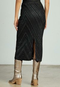 Une jupe midi noire avec un motif en chevrons et des accents métalliques, accompagnée de bottes à talons métalliques.