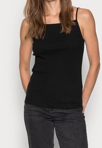 Svart ribbad linne med tunna axelremmar, med fyrkantig halsringning och smal passform. Kombinerat med mörkgrå jeans.