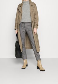 Beige trenchcoat över grå turtleneck, rutiga byxor och beige ankelstövlar. Inkluderar en svart tote-väska. Slät tyg och strukturerad design.