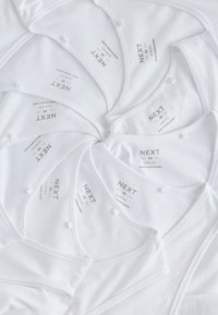 Débardeurs blancs slim fit étiquetés "NEXT M" disposés en motif circulaire sur un fond blanc.