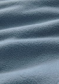 Világoskék bolyhos anyag finom, texturált felülettel lágy hullámokkal és redőkkel jelenik meg, kiemelve puha, meleg tulajdonságait.