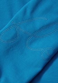Un tessuto turchese con una texture liscia presenta ricami blu in un motivo a spirale, aggiungendo dimensione e interesse visivo.