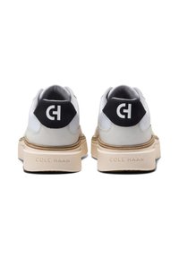 Vita lädersneakers med svarta mocka-hälar och en framträdande vit logotyp. Sulan är krämfärgad med en strukturerad yta.