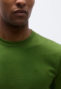 Πράσινο βαμβακερό μπλουζάκι με στρογγυλή λαιμόκοψη, που διαθέτει διακριτικό κεντητό λογότυπο στο ίδιο χρώμα στο στήθος. Ομαλή υφή.