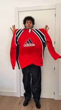 Roter Adidas Oversized-Sweatshirt mit blauen Streifen, gerippter Textur, Logo auf der Brust, getragen mit dunklen Jeans und schwarzen Schuhen.