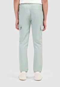 Lichtgroene cargo broek met een relaxte pasvorm, voorzien van zijzakken, een elastische tailleband en een gladde textuur. Draagt een paar witte sneakers.