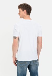 Hvid bomulds T-shirt med korte ærmer, en rund hals og en glat tekstur. Synlig tatovering på armen. Båret med ensfarvede blå denimjeans.
