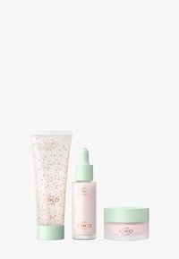 Tre hudpleieprodukter i pastellinnpakning: et rør for rensemiddel med rosa detaljer, en serumflaske med pipette, og en kremkrukke, alle med mintdetaljer.