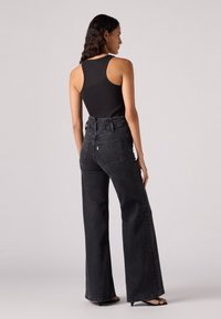 Hoge taille, wijde poot zwarte denim jeans met een gestructureerde afwerking, voorzien van twee achterzakken en gestikte naden.