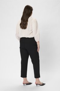 Hellrosa Bluse mit Puffärmeln und strukturiertem Muster, kombiniert mit schwarzen, taillierten Hosen und schwarzen, hochhackigen Mules. Elegante Silhouette.