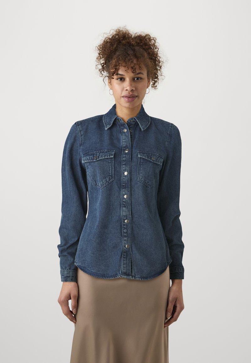 Mørkeblå denimskjorte med naturlig krage, knappelukking, to brystlommer og lange ermer. Stoffet har en myk, noe teksturert finish.
