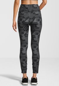 Leggings neri con un motivo geometrico grigio, vita alta e una texture liscia. Abbinati a scarpe nere.