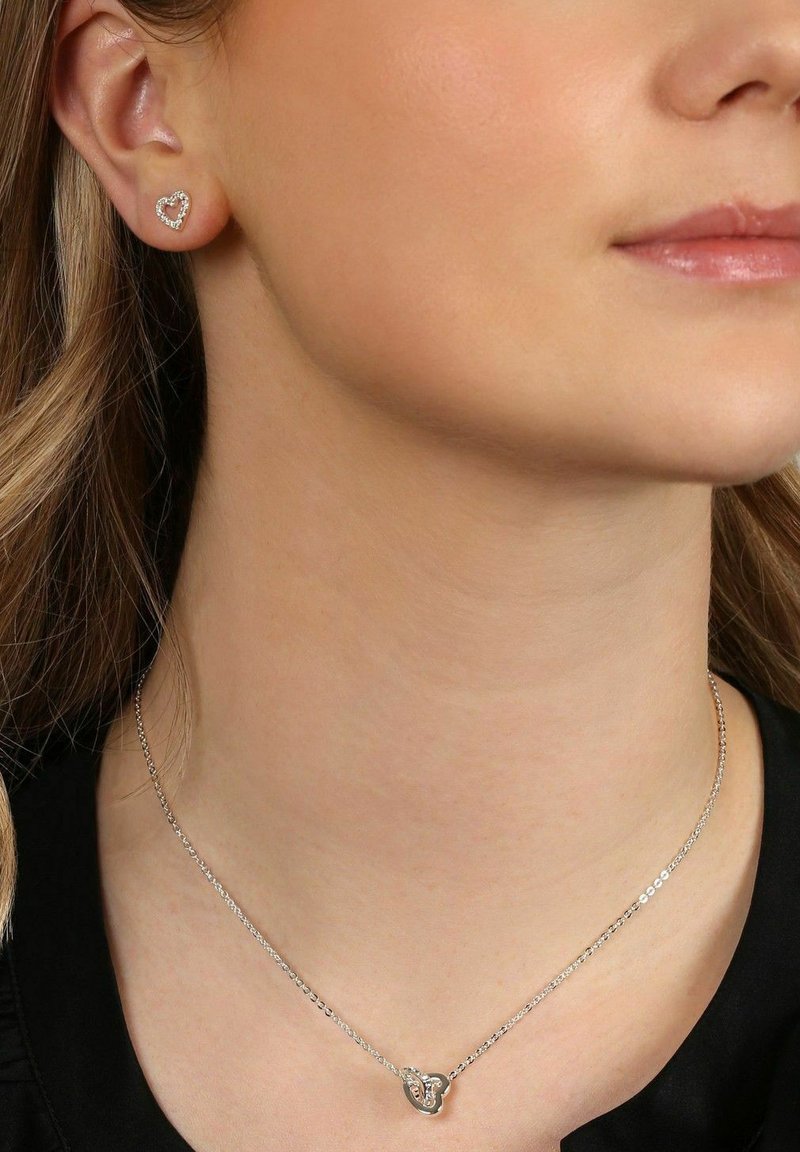 Sölvördade hjärtformade stiftörhängen med klara stenar på ena örat och ett matchande delikat hjärtformat hängsmycke.