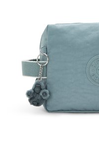 Borsa rettangolare azzurro chiaro con finitura testurizzata, dotata di una tracolla intrecciata, etichetta con logo e un dettaglio di charme in pelliccia staccabile.