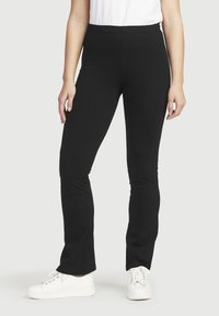 Zwarte stretch leggings met een gladde textuur, voorzien van een strakke pasvorm en een elastische tailleband, gecombineerd met witte sneakers.