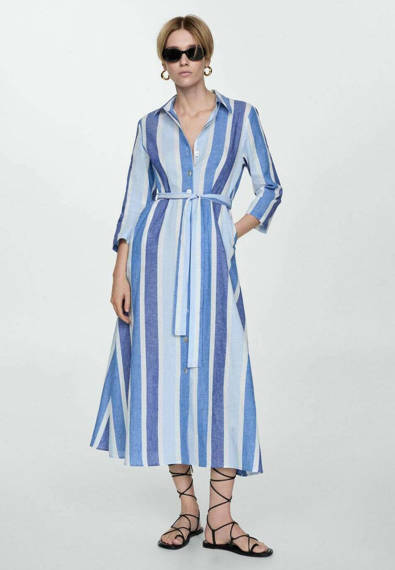 Rochie lungă, cu nasturi, în dungi verticale albastre și bleu deschis. Prezintă mâneci trei sferturi, o curea la talie și buzunare laterale.