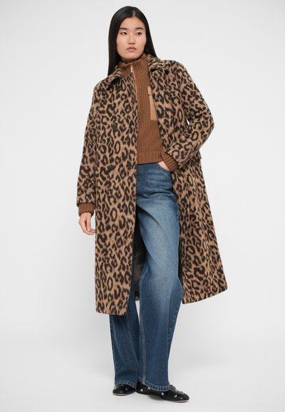 Cappotto in misto lana con stampa leopardata, colletto, chiusura frontale a bottoni e tasche laterali; abbinato a un maglione marrone a coste e jeans blu a zampa.