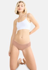 Beige hipsterunderbukser i bomuldsblanding med blonderkant og et logo på venstre side, kombineret med en hvid ærmeløs crop top.