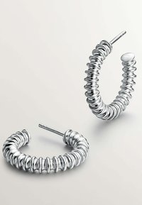 Pendientes de aro de plata con un diseño en espiral, que presentan un acabado suave y extremos redondeados, mostrando un brillo metálico y una superficie texturizada.